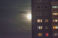 Mond mit zarten Wolken, davor ein Hochhaus mit ein paar dunklen und ein paar erleuchteten Fenstern