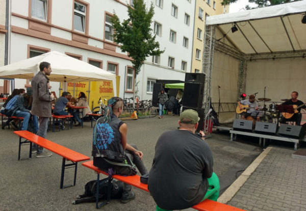 Gäste die zur Bühne schauen, darauf zwei Musiker mit Gitarren, einer singt.