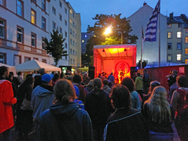 Bild von einigen Metern vor der Bühne über viele Menschen hinweg, die sich das Konzert anhören und anschauen