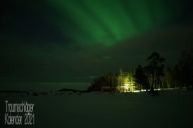 Winterlandschaft im Dunkeln. Am Rand eines Wäldchens steht ein Haus, wirkt wie das typische schwedische rote Holzhaus. Im Vordergrund verschneite Ebene und über dem Haus leuchtet grün das Nordlicht